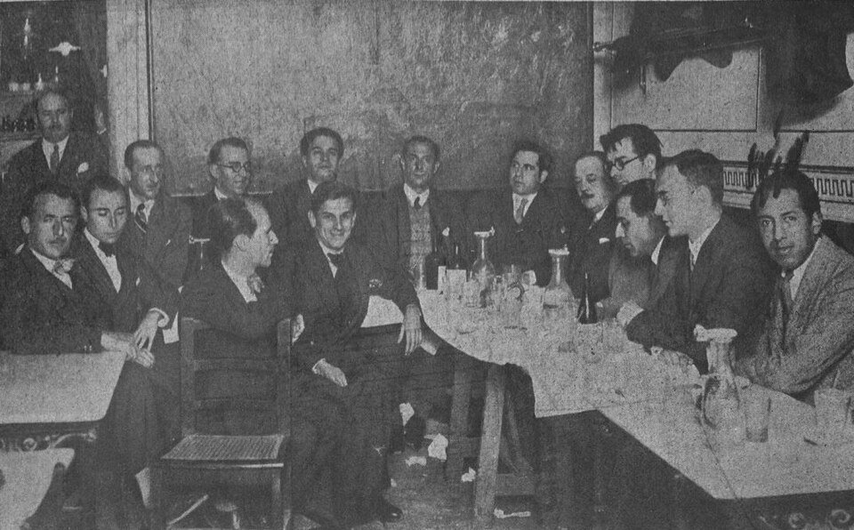 Fotografía antigua de un grupo de hombres sentados alrededor de una mesa en un café